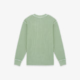 A sage green ribbed knit long-sleeve shirt with white contrast stitching on the shoulders, cuffs, and collar, shown flat against a light gray background.