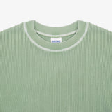 Close-up of a light sage green waffle-knit crewneck sweater with a white ribbed collar trim and a visible neck label reading 'SWEATWEAR'.
