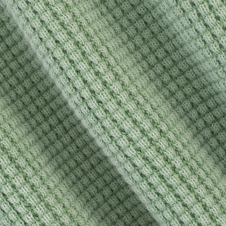 A close-up of a light sage green knit fabric with a textured, ribbed pattern and soft diagonal folds.