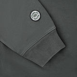 Close-up of a dark gray sweatshirt sleeve with a ribbed cuff and a circular white and black 'Tubble War' patch on the upper arm.