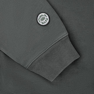 Close-up of a dark gray sweatshirt sleeve with a ribbed cuff and a circular white and black 'Tubble War' patch on the upper arm.