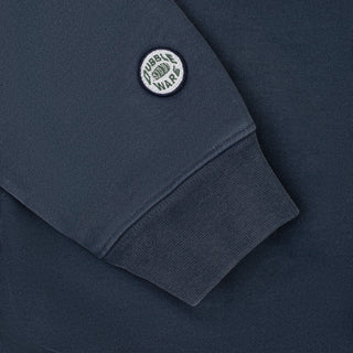 Close-up of a navy blue sweatshirt sleeve with a ribbed cuff and a circular embroidered patch reading 'TUBBLE WAR' on the upper sleeve.