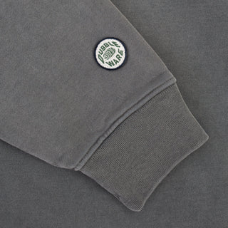 Close-up of a dark gray sweatshirt sleeve featuring a ribbed cuff and a circular embroidered patch that reads 'CUBIK WARS' with a green globe logo.