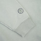 Close-up of a light gray sweatshirt sleeve with a ribbed cuff and a circular embroidered patch reading 'FUEL BURN WARS' on the upper cuff.