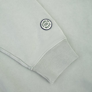 Close-up of a light gray sweatshirt sleeve with a ribbed cuff and a circular embroidered patch reading 'FUEL BURN WARS' on the upper cuff.