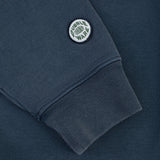 Close-up of a dark slate blue sweatshirt sleeve featuring a circular embroidered 'Dubble Wars' patch on the cuff.