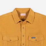 Close-up of a mustard yellow button-up shirt with a pointed collar, two chest pockets, and a visible Dubbleware neck label and a small chest patch logo.