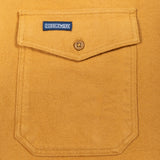 Close-up of a mustard yellow suede or suede-like fabric pocket with a flap closure, a single button, and a visible Doubleware label.