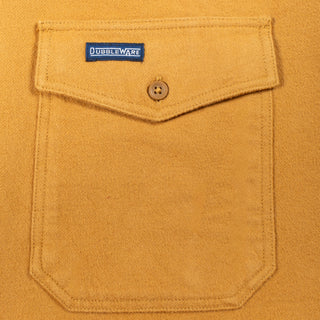Close-up of a mustard yellow suede or suede-like fabric pocket with a flap closure, a single button, and a visible Doubleware label.