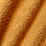 A close-up of textured, fuzzy fabric in a warm mustard yellow or golden ochre color, draped in soft diagonal folds.