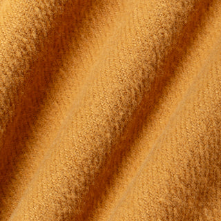 A close-up of textured, fuzzy fabric in a warm mustard yellow or golden ochre color, draped in soft diagonal folds.