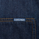 Close-up of dark indigo denim fabric with orange contrast stitching and a small rectangular Dubbleware label near the pocket.