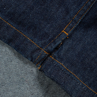Close-up of dark indigo denim fabric with orange contrast stitching and a lighter gray denim section folded over.