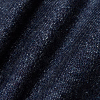 A close-up of dark indigo denim fabric with a visible twill weave and soft folds.