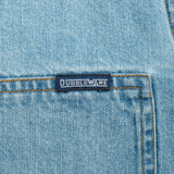 Close-up of a light blue denim garment showing a front pocket with contrast stitching and a small dark brand label reading Dubbleware.