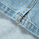 Close-up of light blue denim fabric with orange contrast stitching along a folded seam.