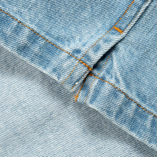 Close-up of light blue denim fabric with orange contrast stitching along a folded seam.
