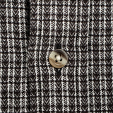 Close-up of a black and white woven fabric with a repeating geometric pattern and a single round metallic button near the center.