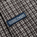 Close-up of a woven knit fabric with a dark brown and off-white textured pattern, featuring a blue embroidered label with the brand name 'OUBLEWARE' in white.