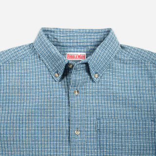 A light blue and white checkered long-sleeve button-down shirt with a chest pocket, displayed flat against a light gray background.