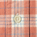Close-up of a plaid fabric with a white button, showing a pattern of coral pink, white, and light blue stripes.