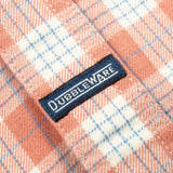 Close-up of a peach and white plaid fabric with a navy blue Dubbleware brand label sewn onto the side.