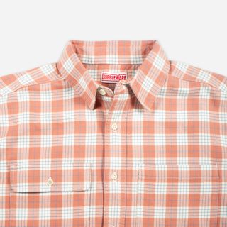 A close-up of a Doubleware button-down shirt featuring a peach-orange and white plaid pattern, with a visible brand label inside the collar.