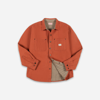An orange long-sleeve button-up shirt jacket with two chest pockets, shown flat on a light gray background. The shirt jacket is slightly open to reveal a beige and brown plaid lining.