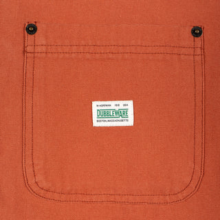 Close-up of a textured orange canvas pocket with a white Dubbleware label stitched in the center, featuring two black snap buttons at the top corners.
