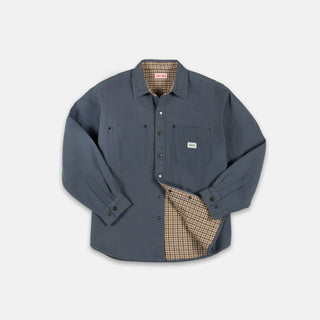 A slate blue work shirt with a beige and brown checkered lining, shown on a light gray background. The shirt features two chest pockets, a button-down front, and the brand label on the left chest pocket reads 'Fjäl'.