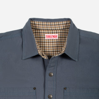 Close-up of a Doubleware button-up shirt in slate blue, showing the inner plaid lining of the collar and the brand label.