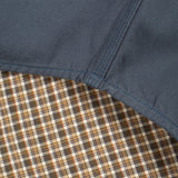 Close-up detail of a garment showing a dark slate blue fabric panel stitched over a brown, beige, and white plaid lining.
