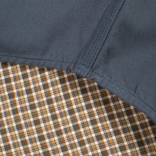 Close-up detail of a garment showing a dark slate blue fabric panel stitched over a brown, beige, and white plaid lining.
